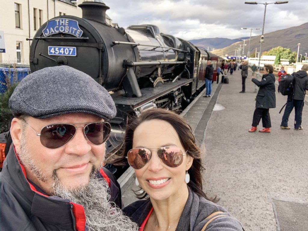 couple poses by train during trip to Scotland