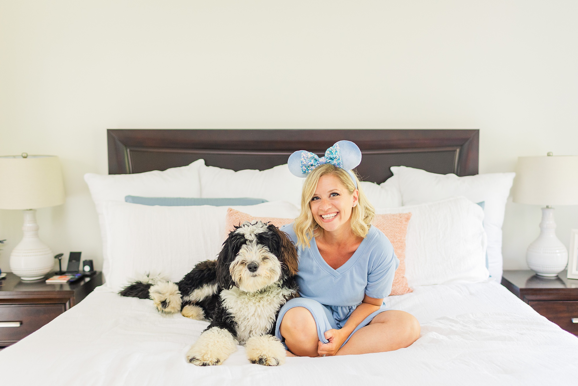 business owner sits on bed with dog and blue Mickey ears