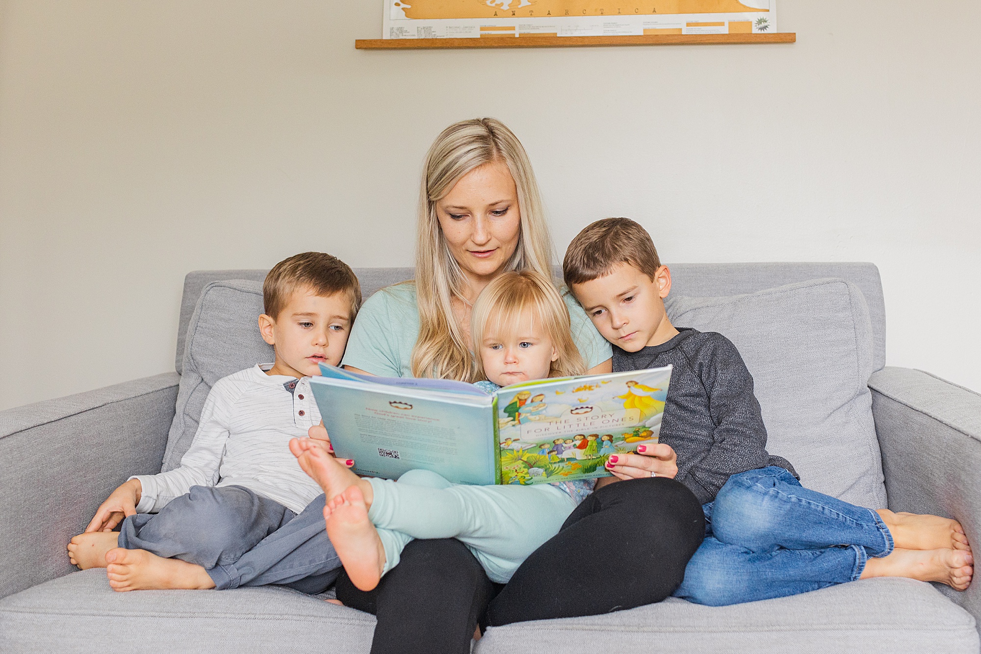 mom reads book to three kids on couch