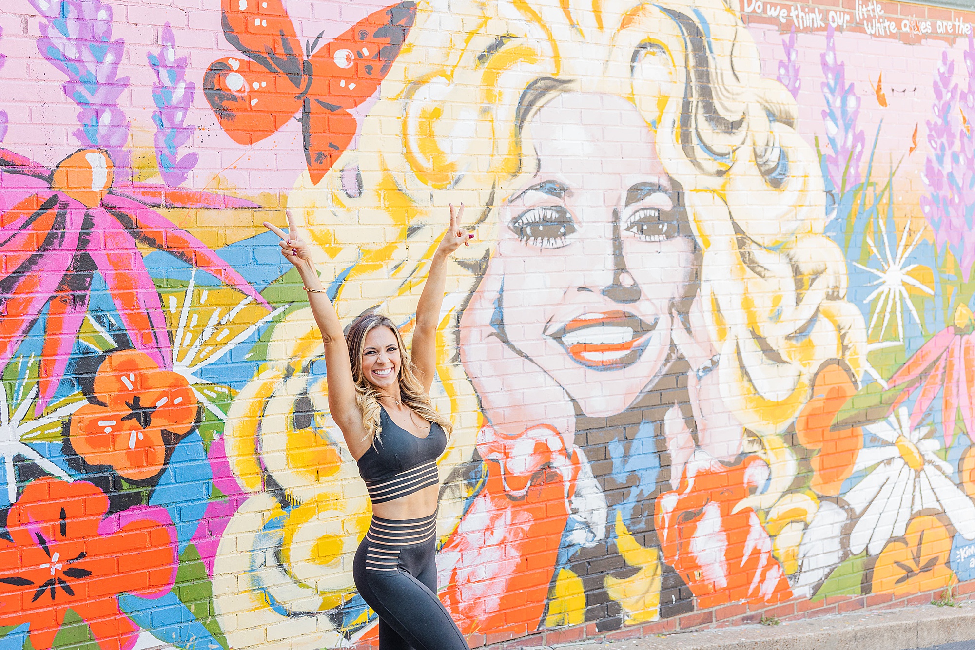 woman poses by Dolly Parton mural during fitness coach branding session