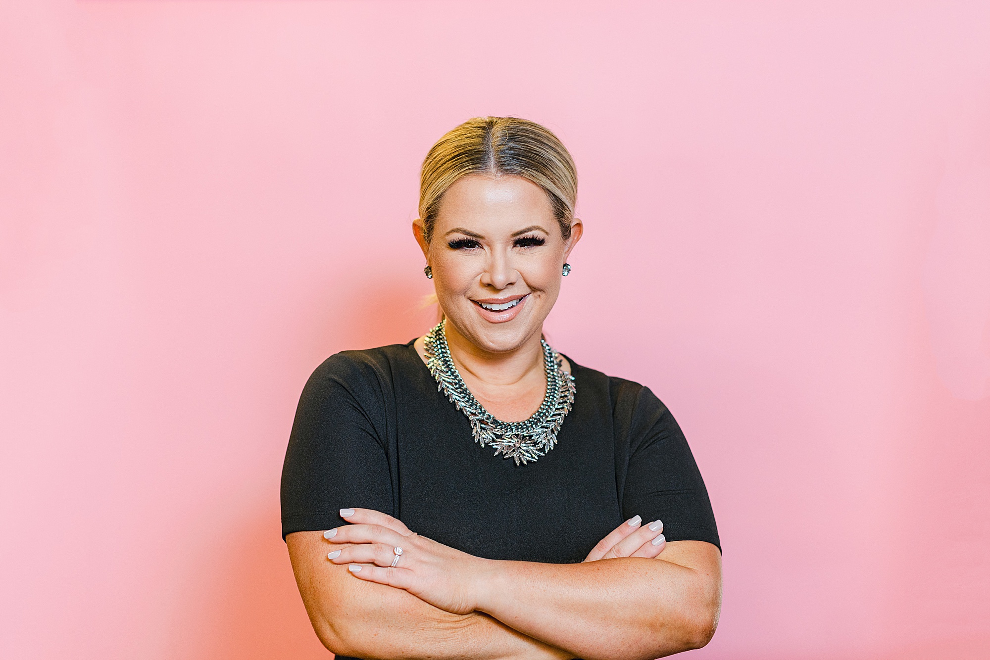makeup artist poses in front of pink wall with arms crossed during Nashville branding photos