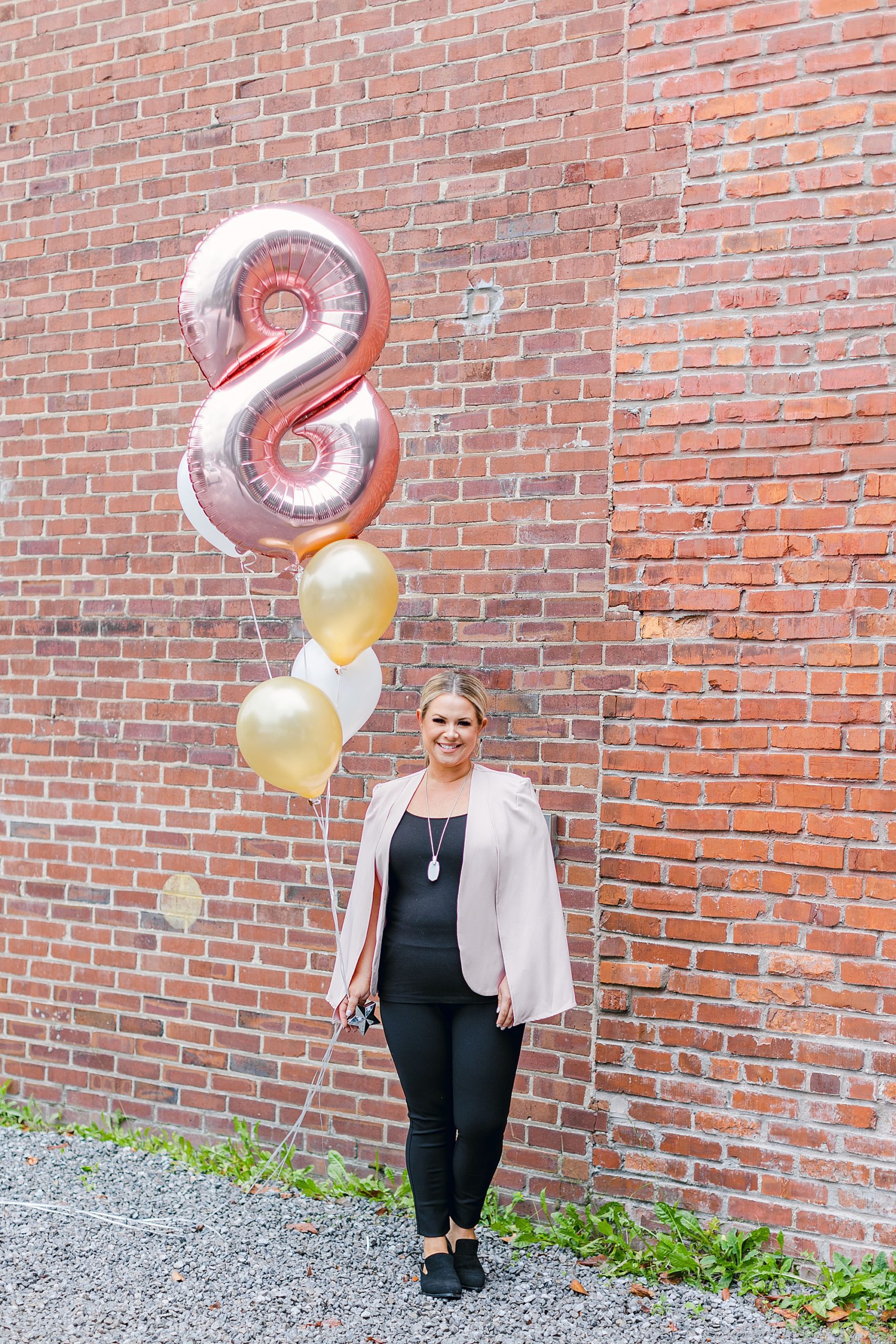 Nashville esthetician and beauty expert holds 8 balloon against brick wall in Nashville TN
