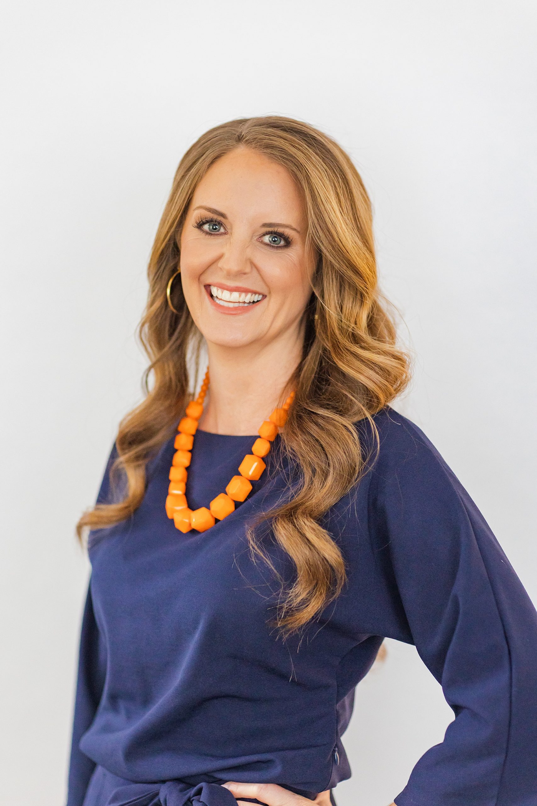 woman poses in blue top with chunky orange necklace