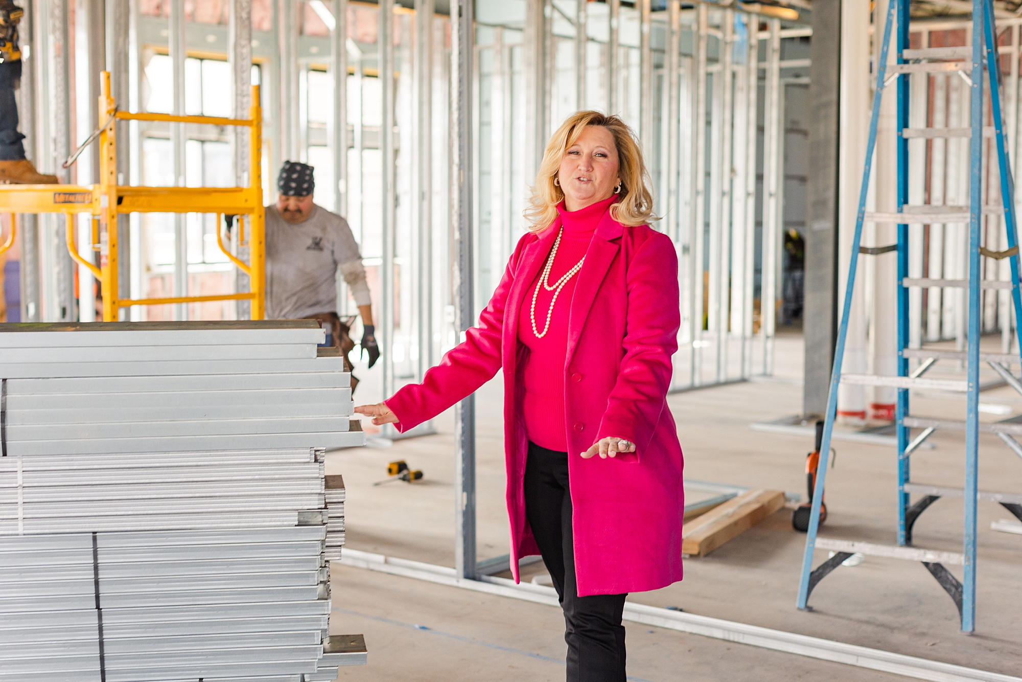 woman in pink coat stands inside The Sapphire Suite during construction