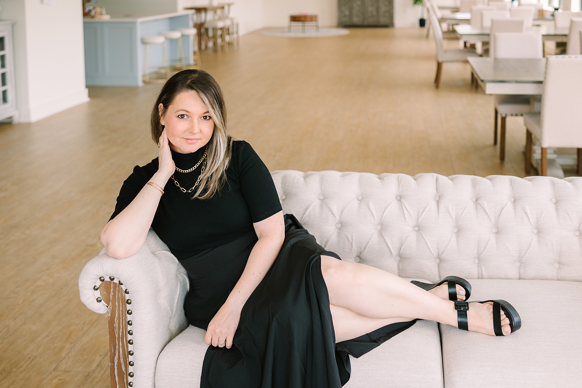 woman sits on couch in black dress and skirt during Sapphire Suite branding session