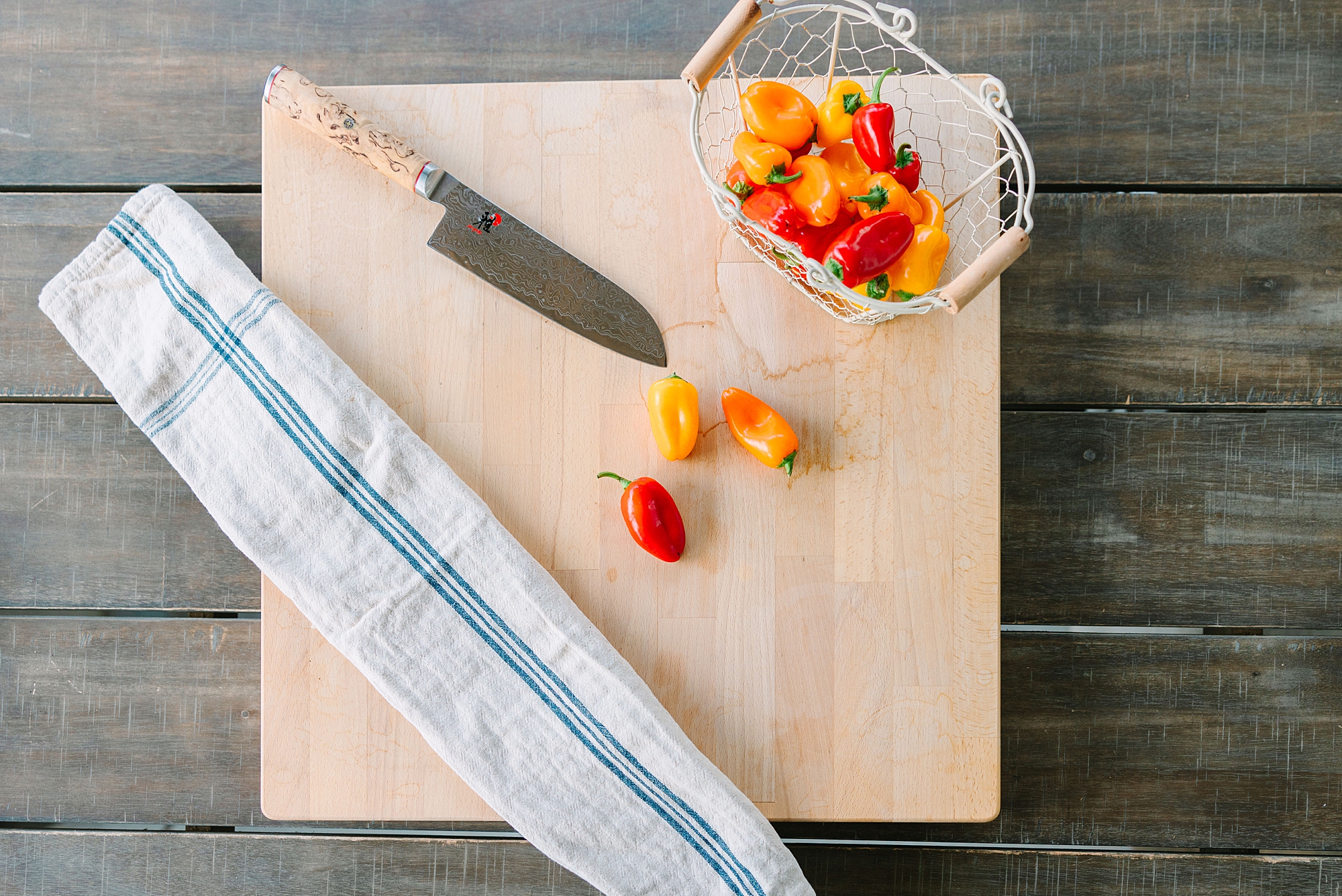 red and orange peppers lay on wooden cutting board with knife