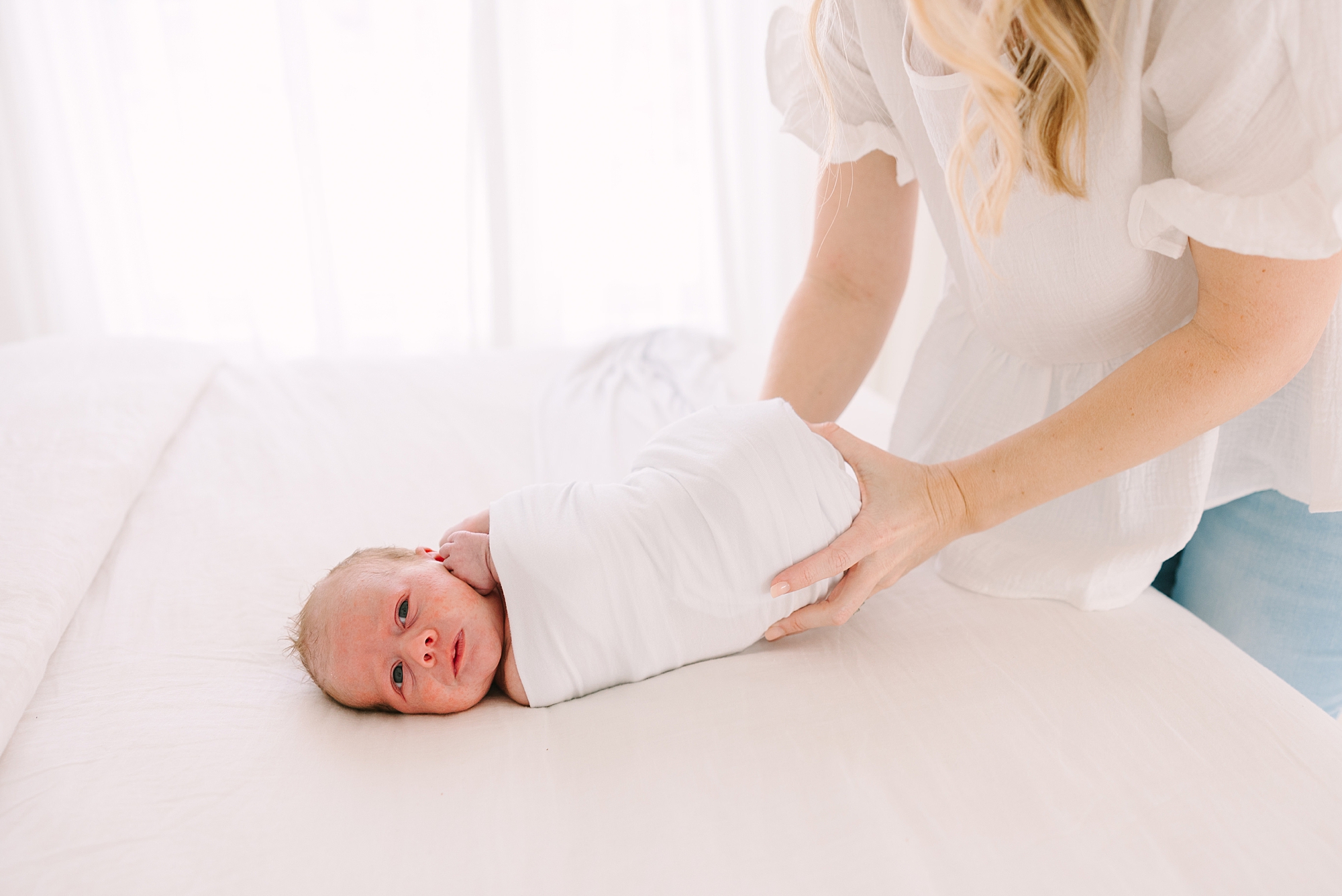 newborn photographer swaddles baby in white wrap