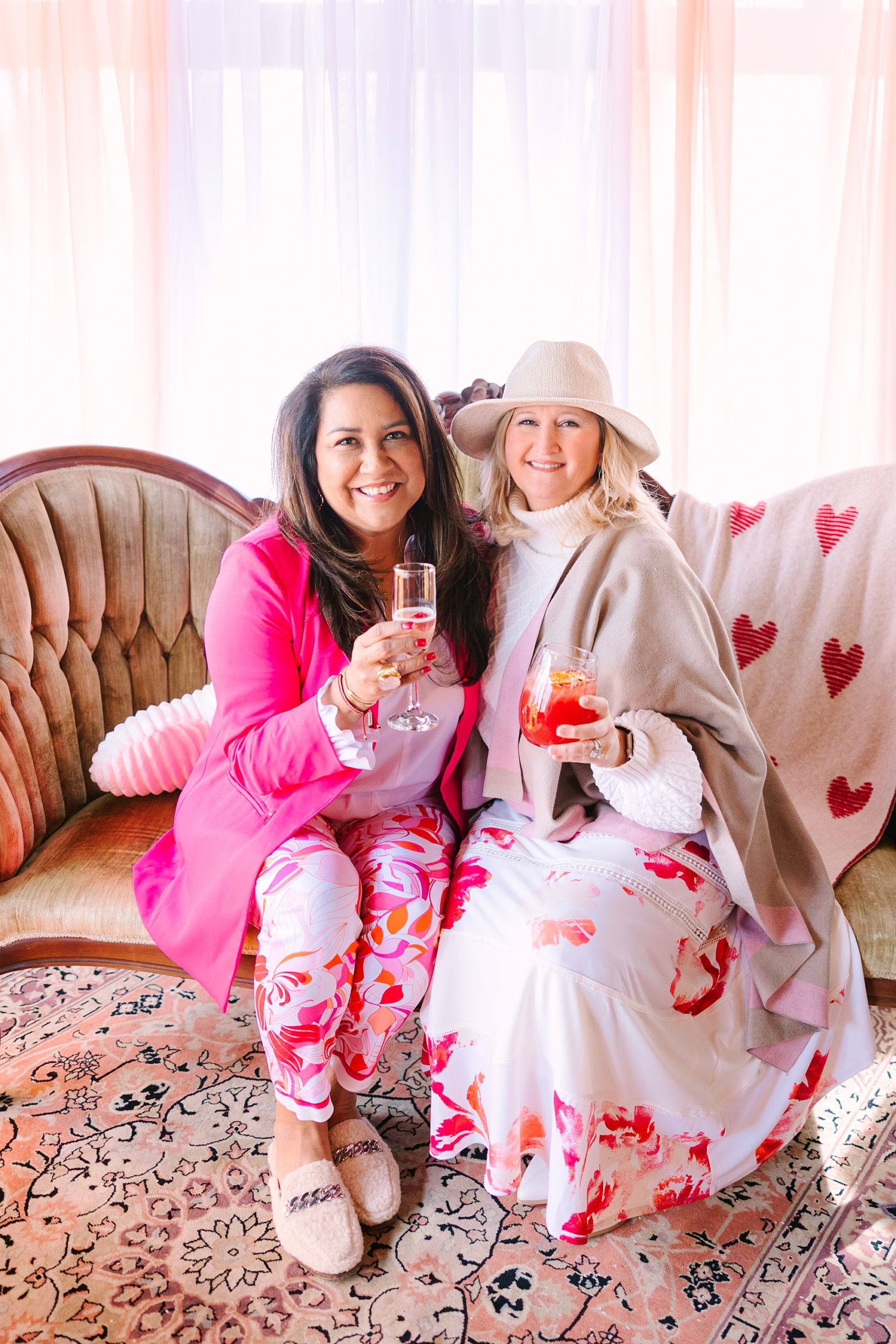 woman in pink blazer sits on couch wit woman in pink and white dress