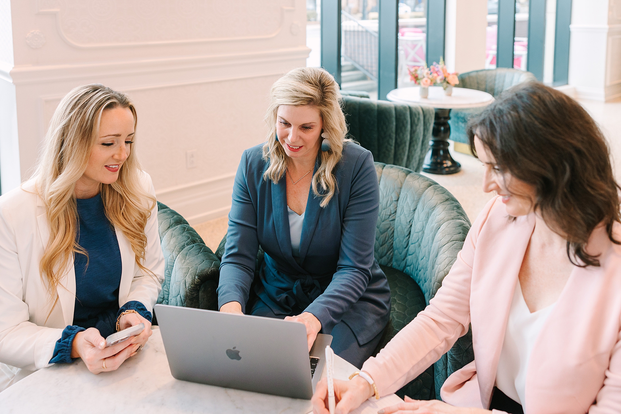 woman in blue sweater types on computer while two women talk to her