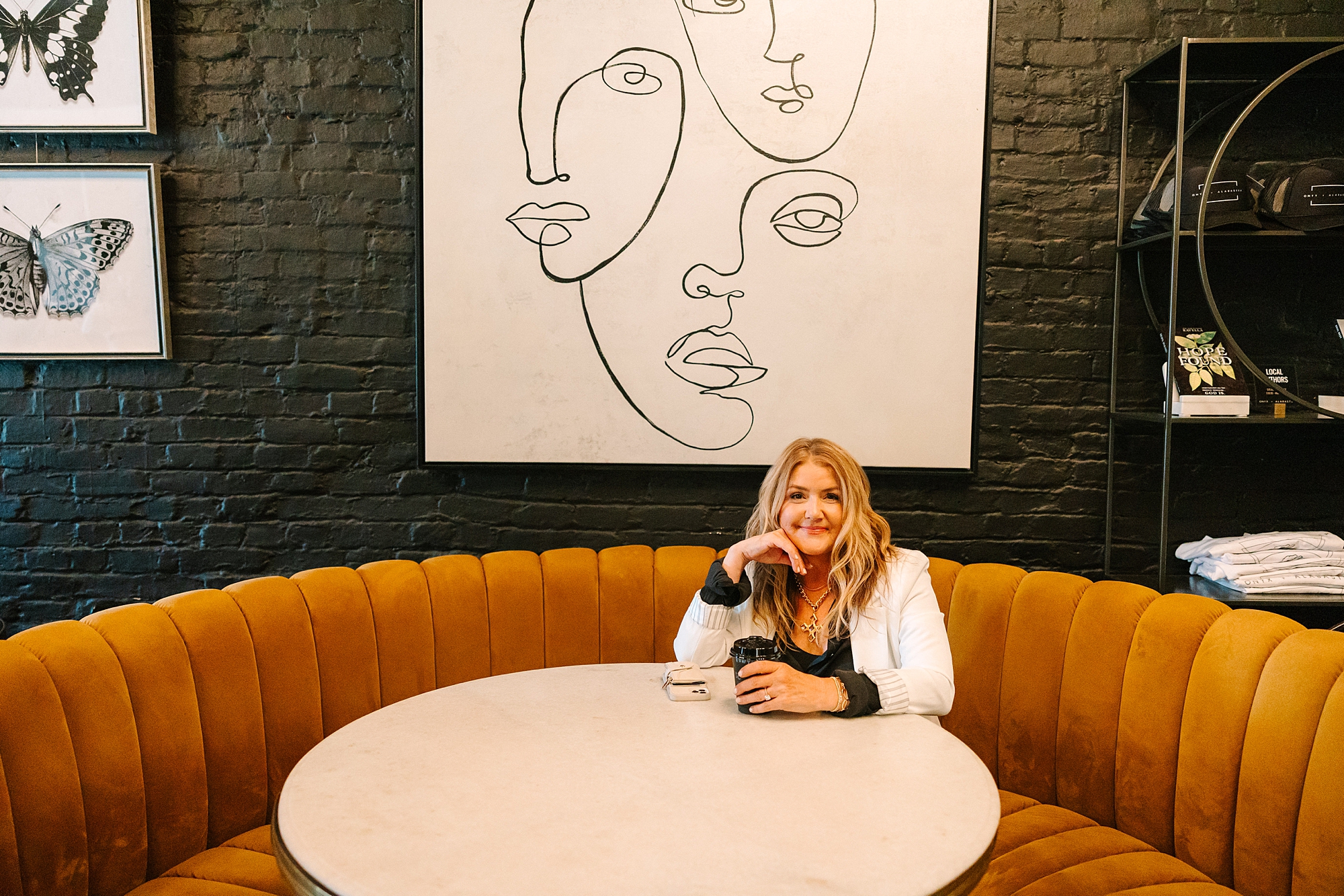 blonde woman in white jacket sits on orange sofa in Franklin TN coffee shop