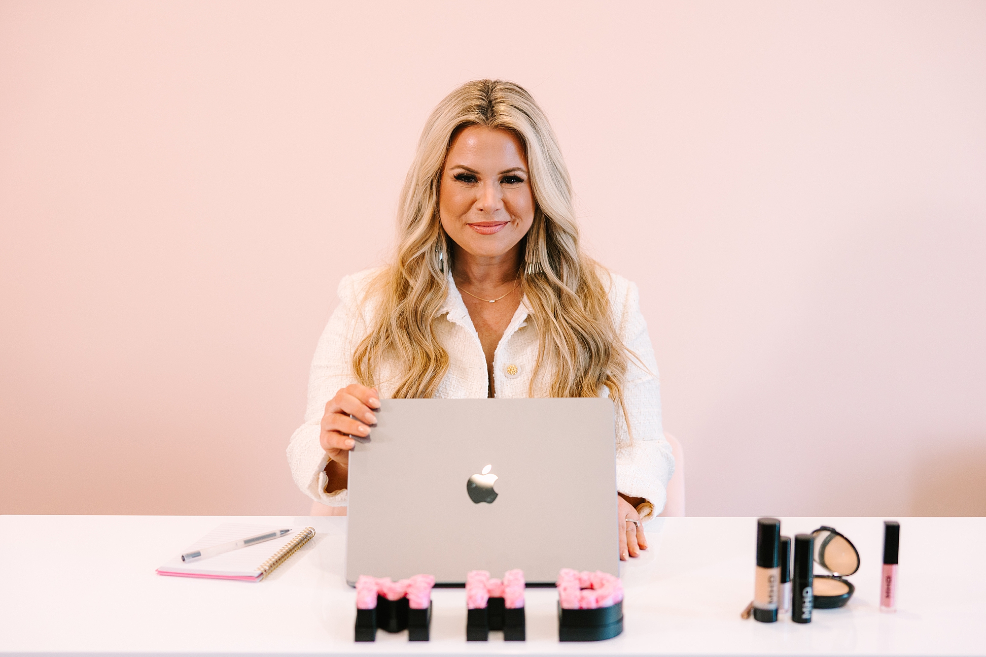 woman sits with laptop and makeup products on desk