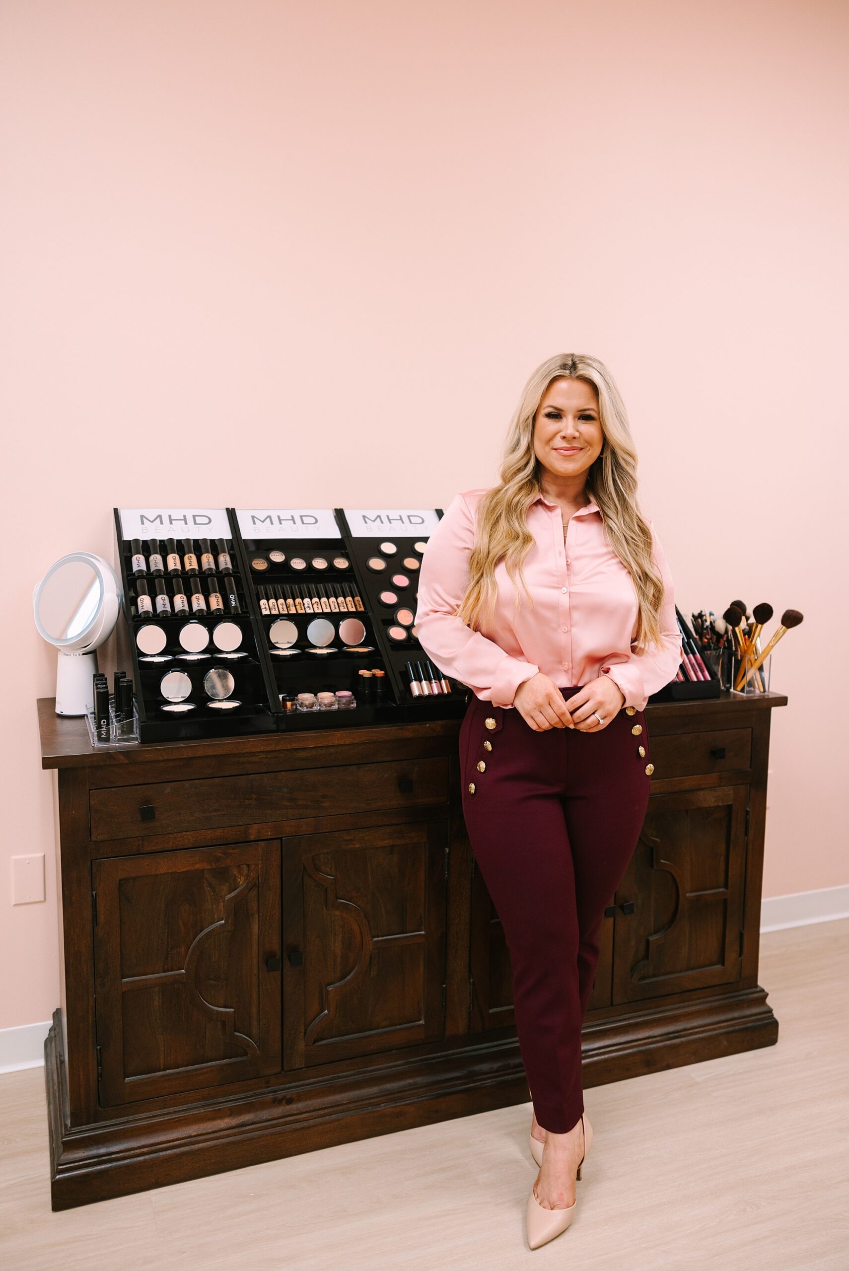 blonde woman in pink top leans against lipstick display in salon
