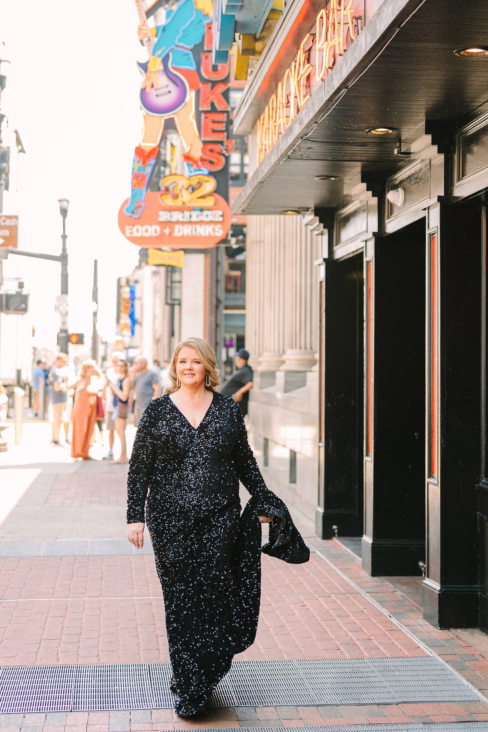 woman picks up skirt on black dress walking down Broadway in Downtown Nashville
