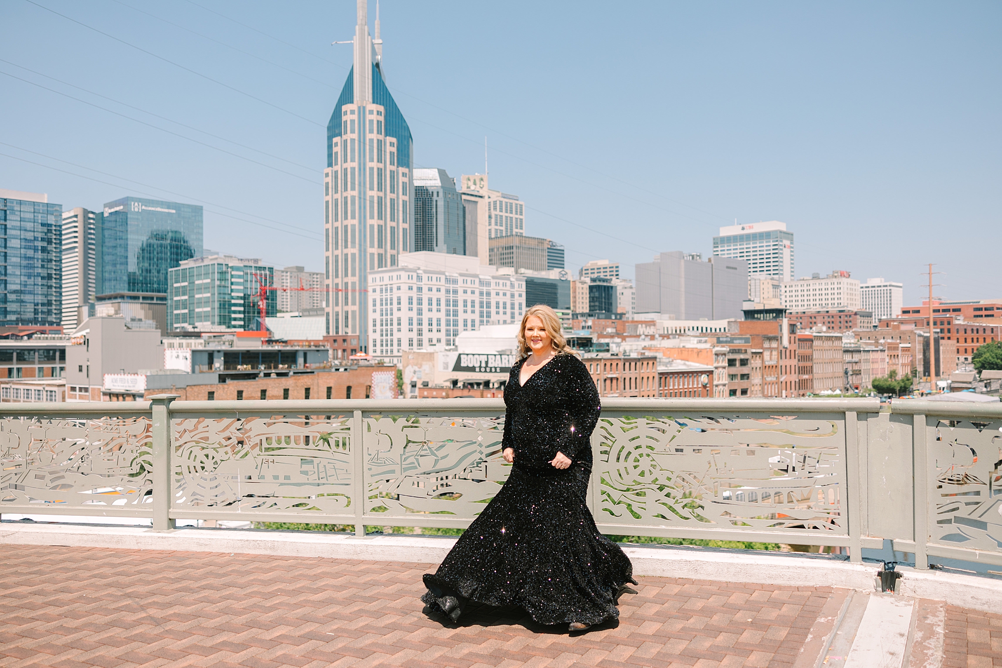 woman poses on downtown Nashville pedestrian bridge in front of Nashville skyline