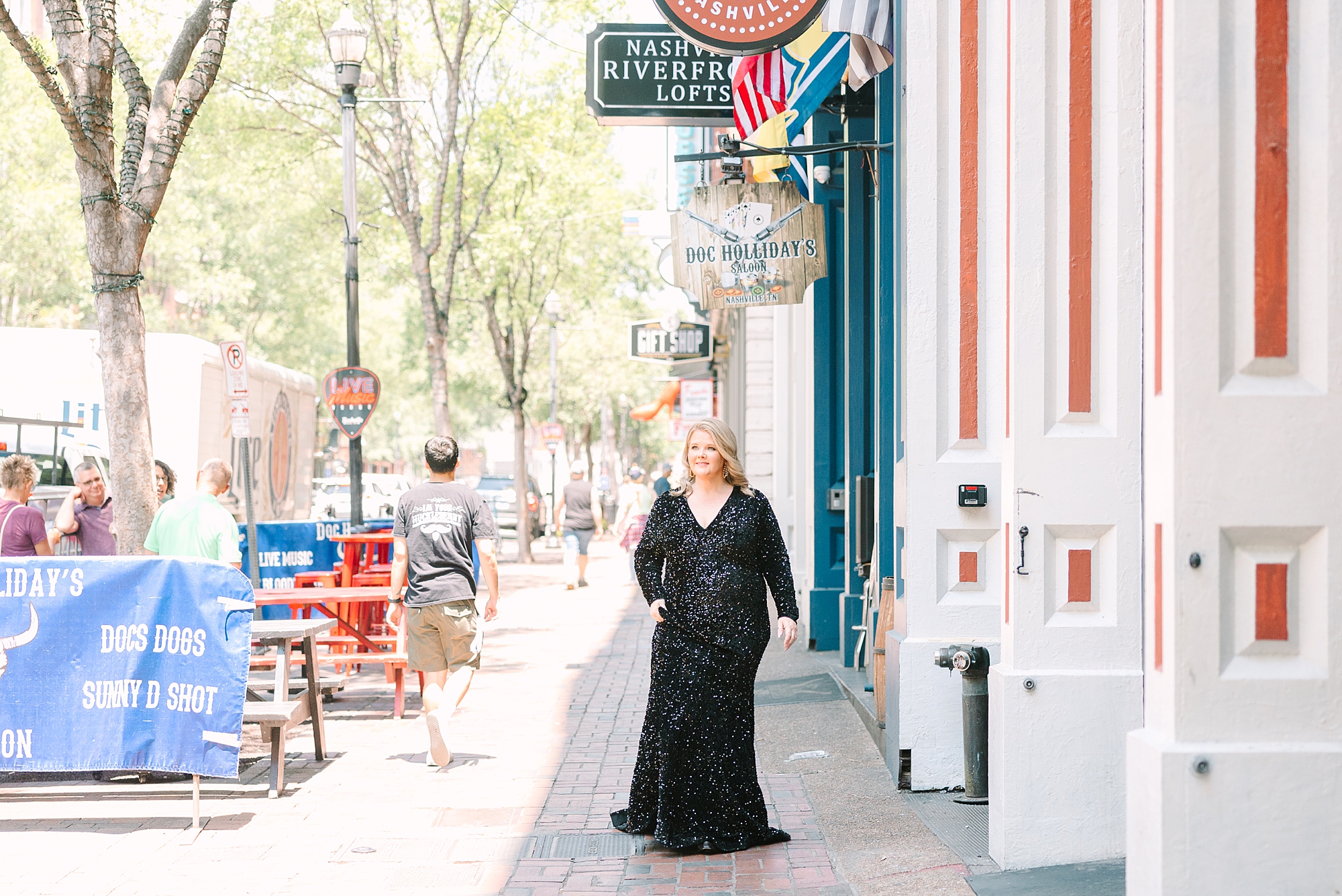 woman walks down woman in black dress smiles in front of large blue doors on Broadway in Downtown Nashville in black dress