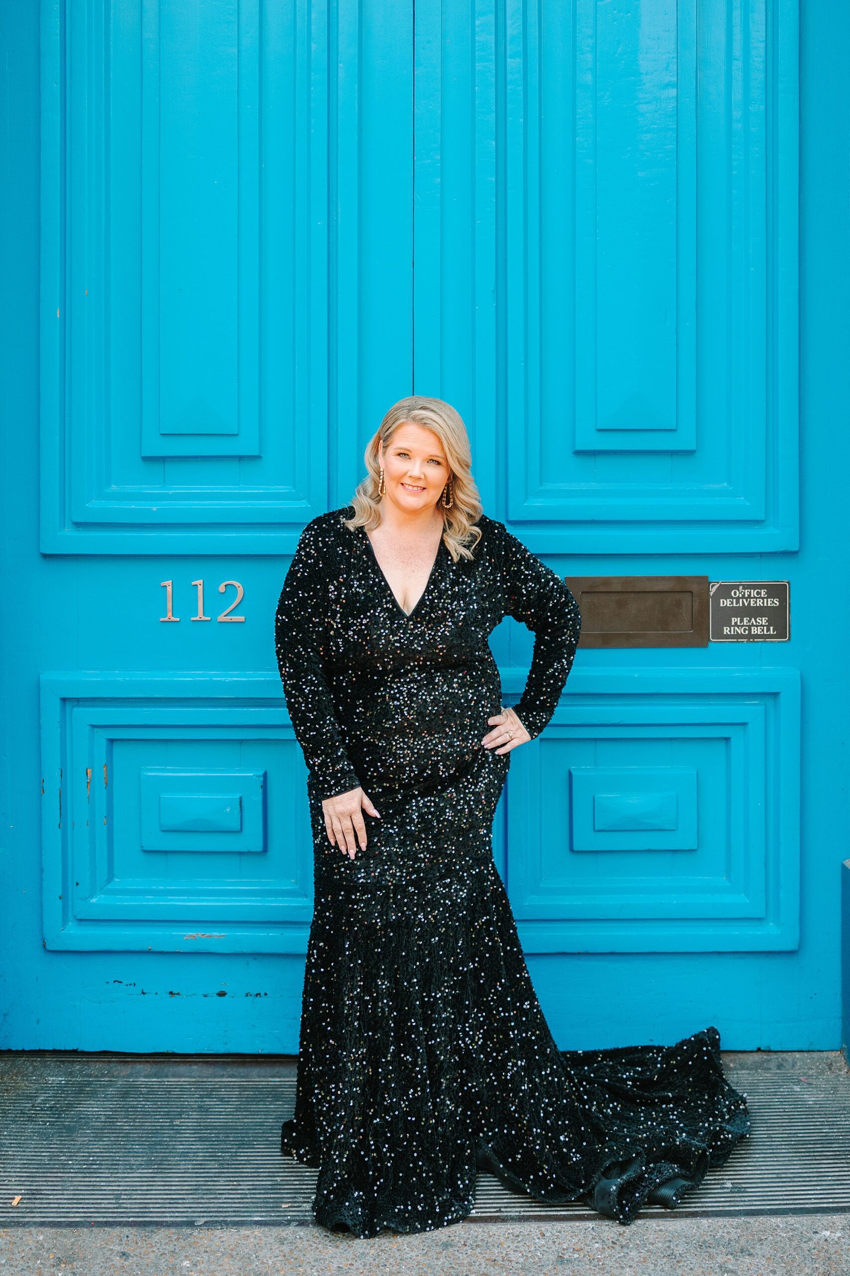 woman in black dress smiles in front of large blue doors on Broadway in Downtown Nashville