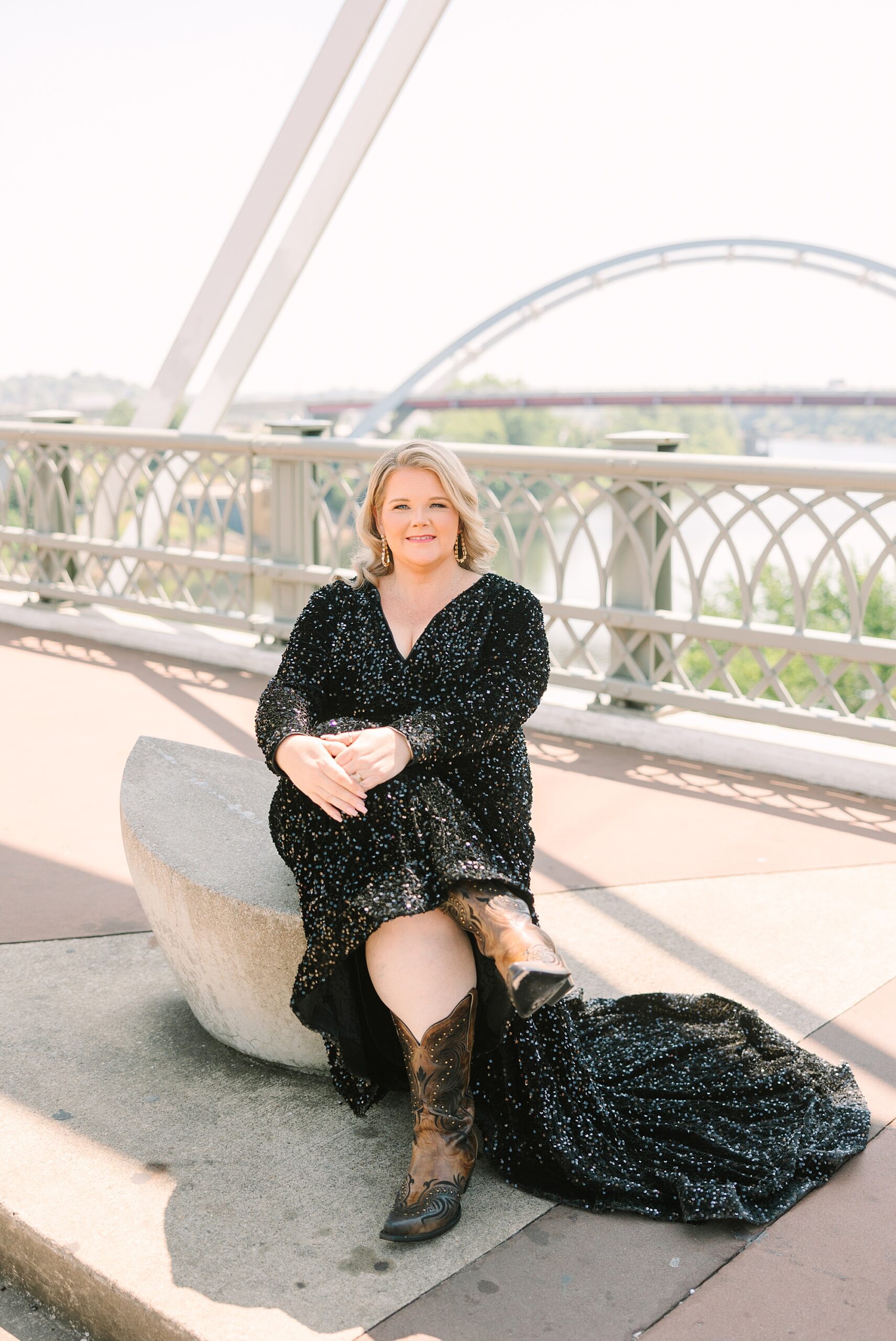 woman sits on Nashville pedestrian bridge showing off cowboy boots