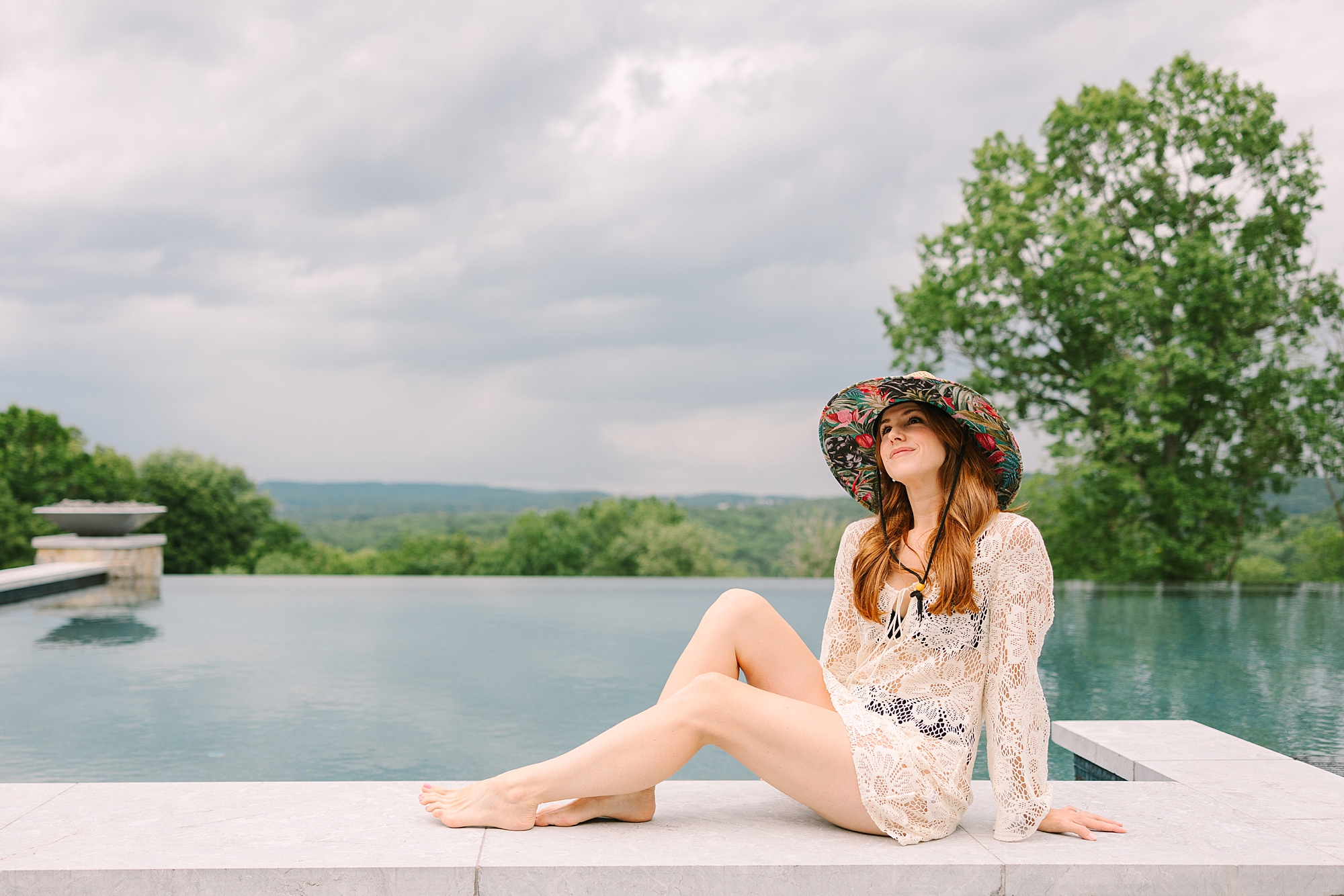 redhead woman sits on edge of pool with beach hat