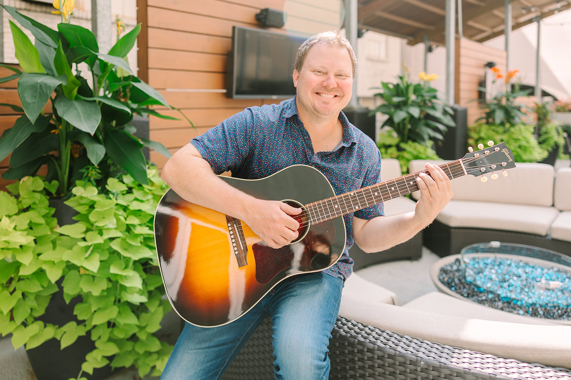man sits on patio furniture playing guitar during branding photos in Downtown Nashville