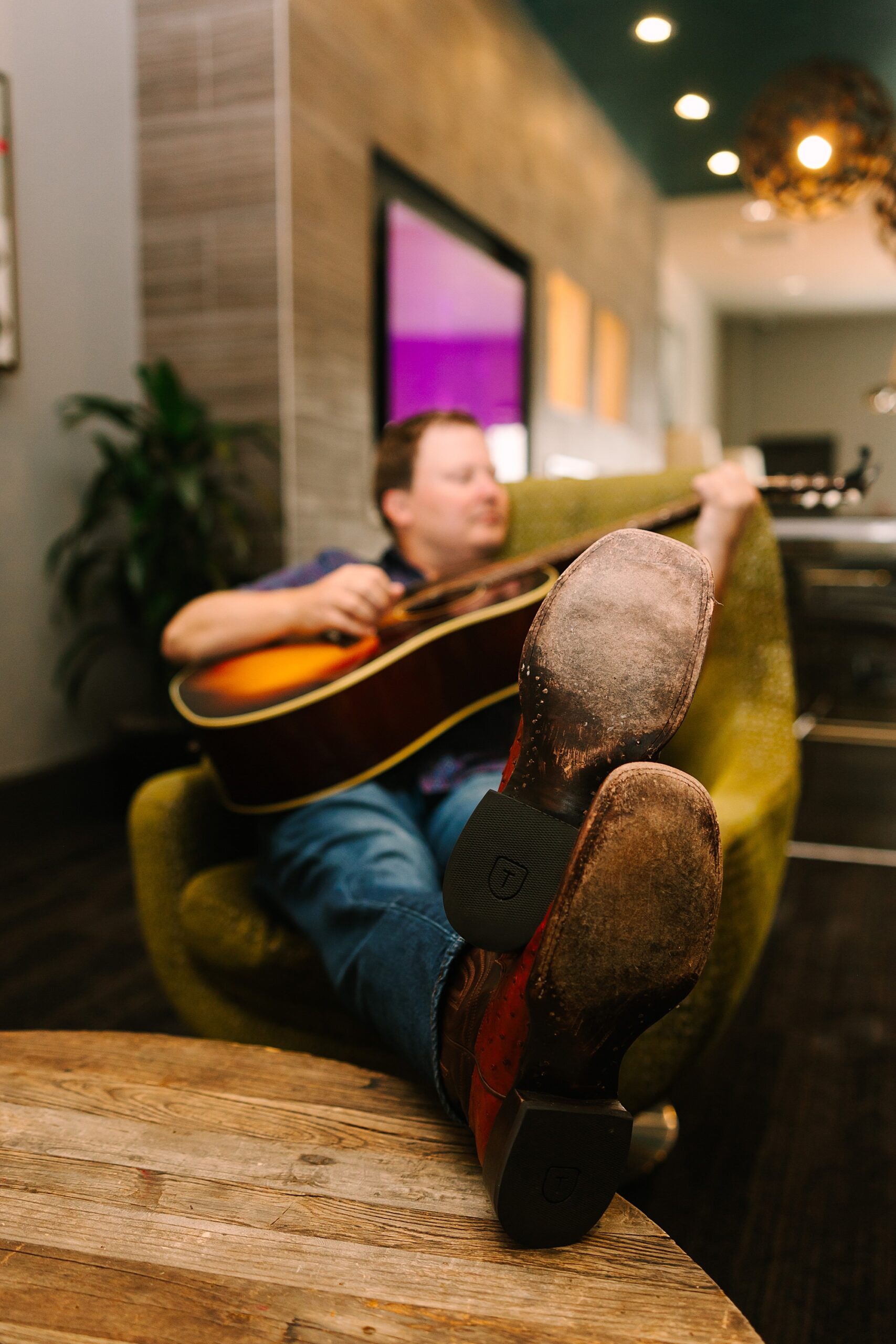 man sits in chair with feet on table playing guitar during Downtown Nashville branding session