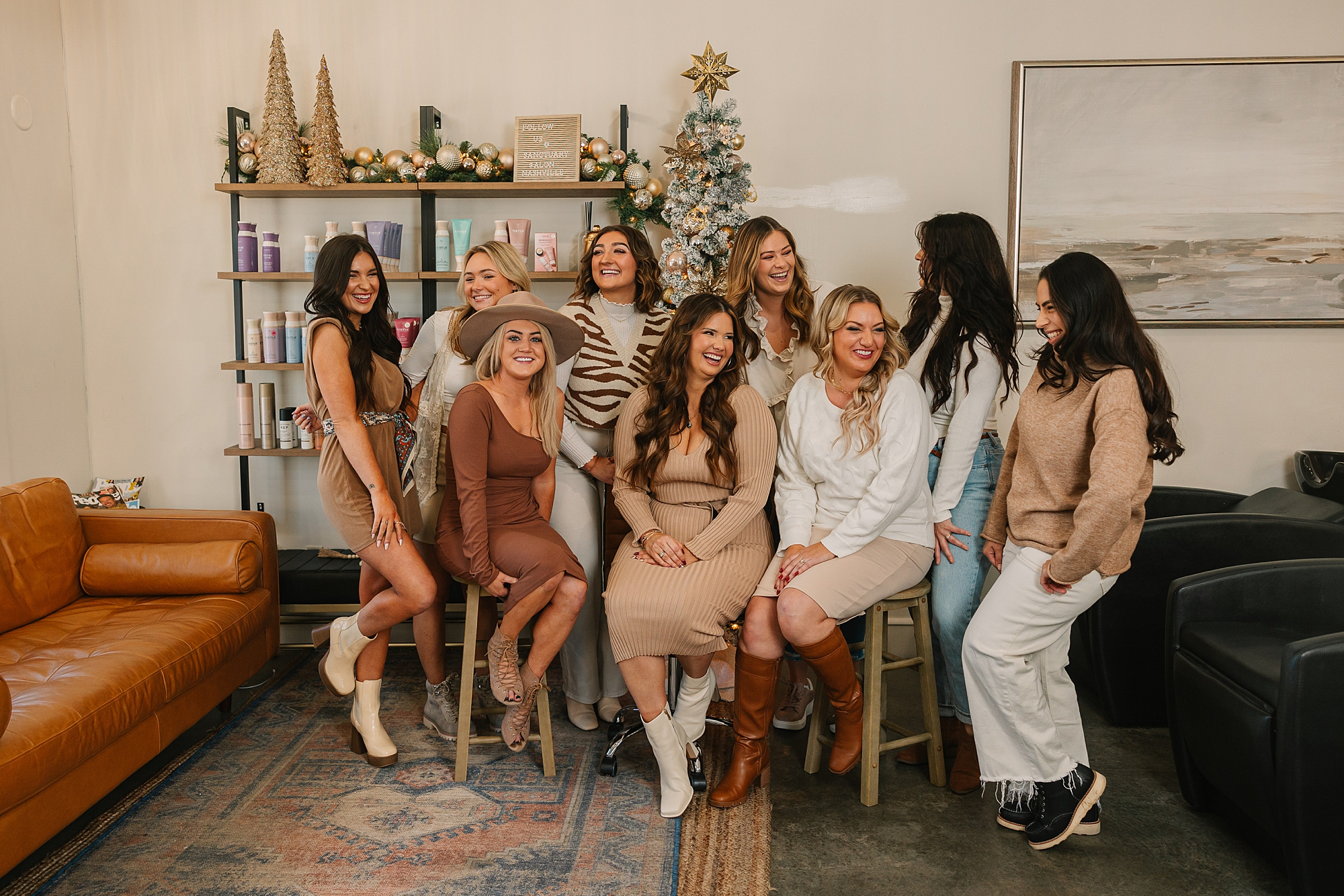 team of stylists sit and stand together by Christmas tree for seasonal branding photos