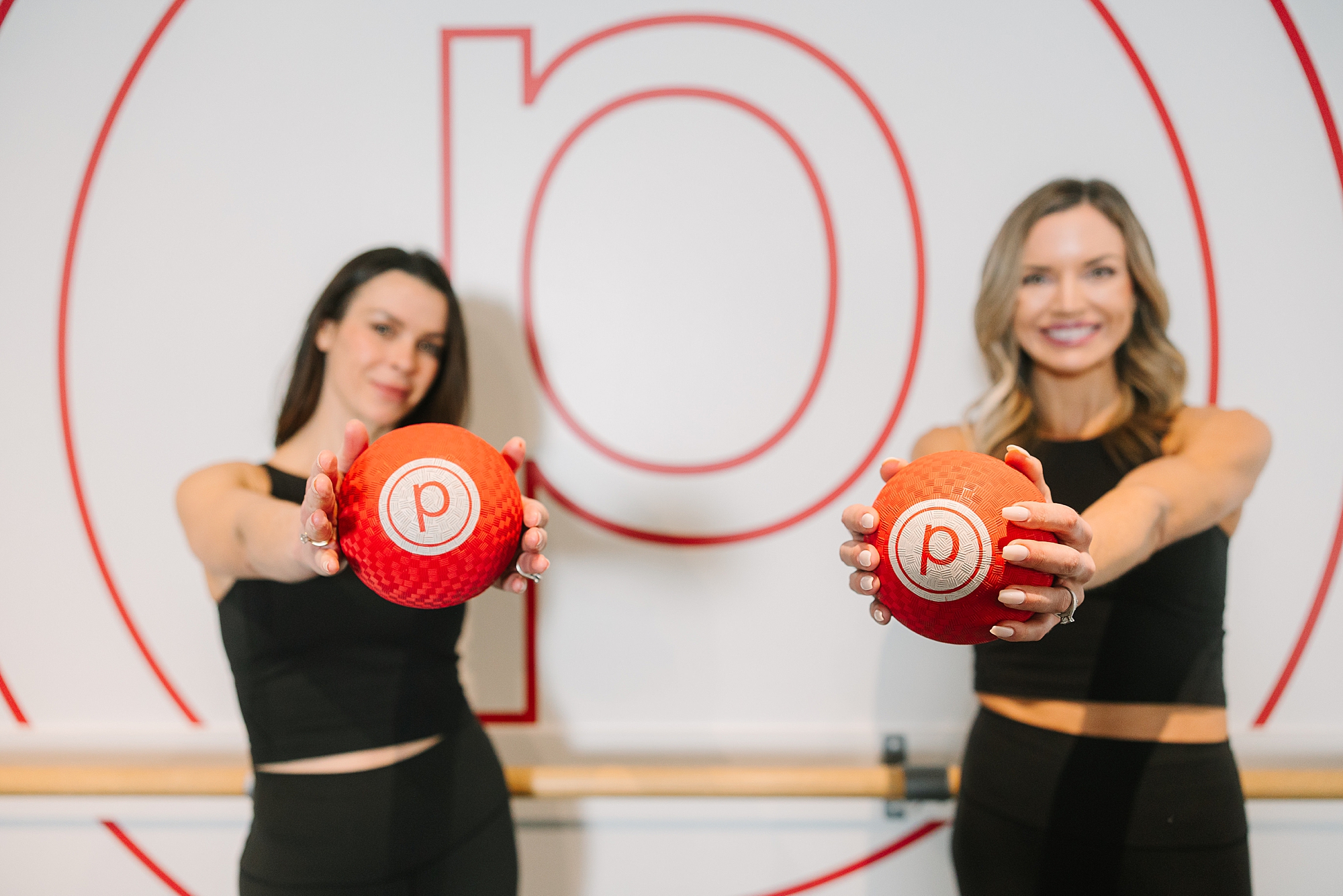 women hold out red pure barre weighted balls