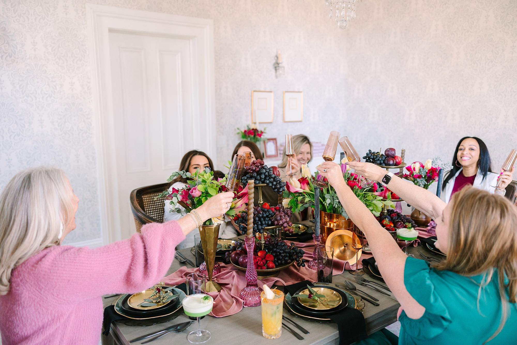 women reach across table to toast drinks